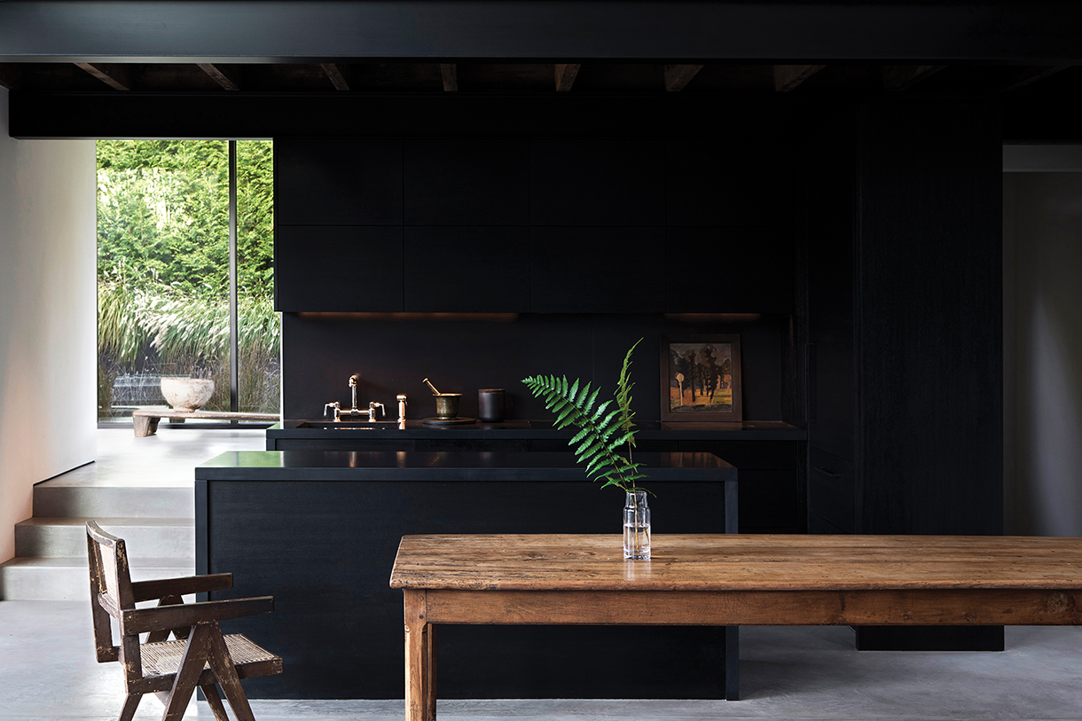 Modern farmhouse kitchen with black stained walls, cabinets and countertop with rustic natural farm table as a centerpiece. 